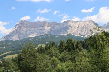 Fototapeta na wymiar Coravara, Italy-July 16, 2022: The italian Dolomites behind the small village of Corvara in summer days with beaitiful blue sky in the background. Green nature in the middle of the rocks.
