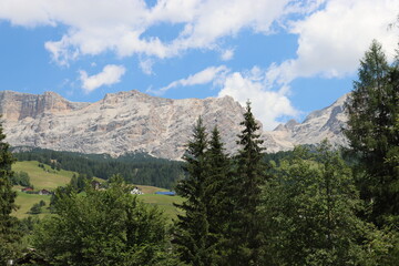 Obraz premium Coravara, Italy-July 16, 2022: The italian Dolomites behind the small village of Corvara in summer days with beaitiful blue sky in the background. Green nature in the middle of the rocks.