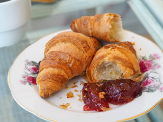 Croissant with marmalade and cup of coffee. Brocken croissant. Vintage style, aesthetic. 
White cup...