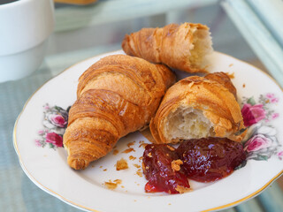 Croissant with marmalade and cup of coffee. Brocken croissant. Vintage style, aesthetic. 
White cup with a transcription 