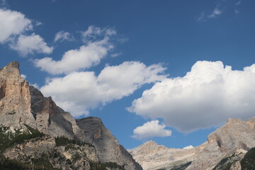 Fototapeta premium Coravara, Italy-July 16, 2022: The italian Dolomites behind the small village of Corvara in summer days with beaitiful blue sky in the background. Green nature in the middle of the rocks.