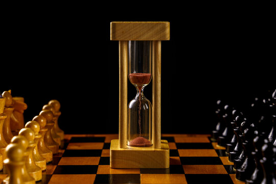 Hourglass in the center of the chessboard, black and white pieces. Soft focus, copyspace