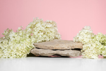 Stone Podium with flowering hydrangea branches for product presentation. Abstract minimal natural rock pedestal on pink background. Showcase, white flowers soft shadow. Scene, display case. Front view