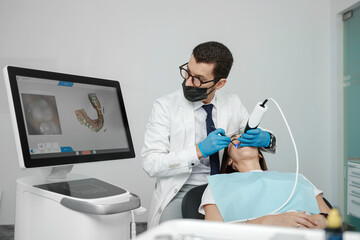 Male orthodontist scaning patient with dental intraoral scanner and controls process on screen.