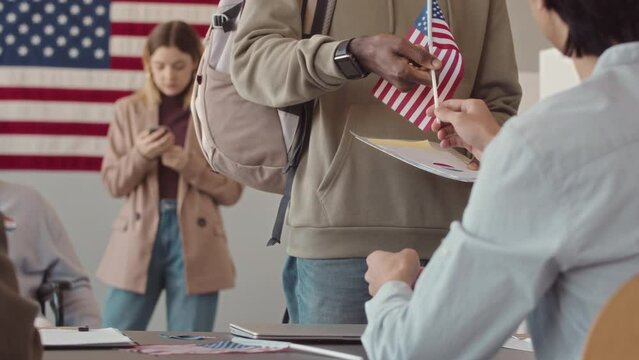 Rear view slowmo of workers giving US flags, vote stickers and ballots to diverse people came to vote to local voting station at electoral district