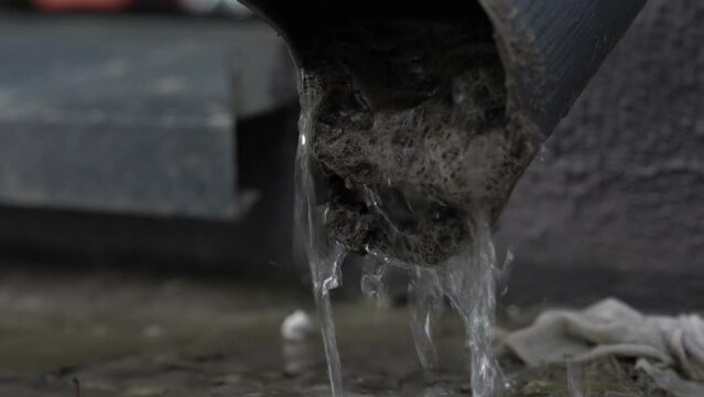 Melting water flowing from steel downpipe at city pavement close view