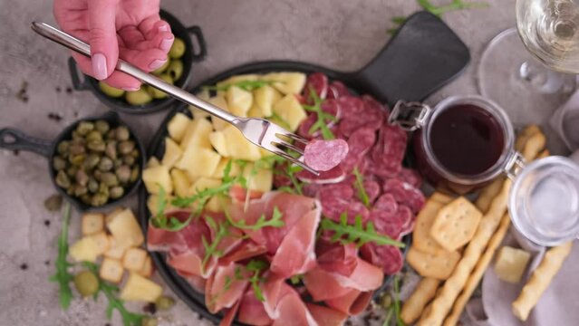 meat and cheese plater at domestic kitchen - woman pricks slice of fuet sausage on a fork