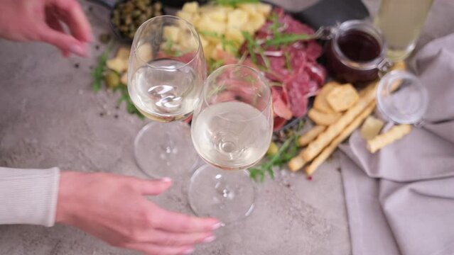 woman putting two glasses of wine to table with meat and cheese plater at domestic kitchen