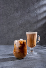 Ice coffee in a tall glass with cream poured over and coffee beans. Cold coffee drink on a dark background with copy space. Set with different types of coffee drinks on a dark table.