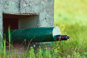 A green machine gun sticks out of a World War II military bunker. Young green grass.