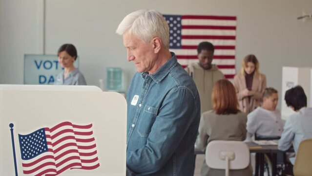 Medium slowmo of diverse men and women with ballots coming to vote booth to go through procedure of voting on Elections Day