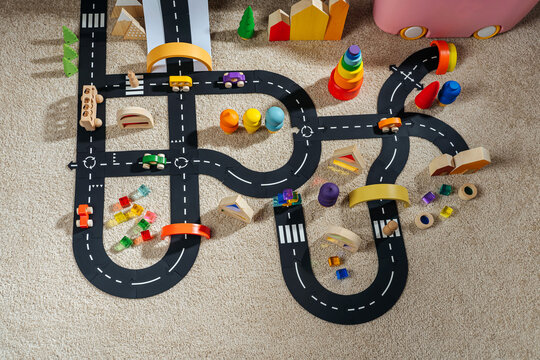 A toy town built in a children's room. Car track, toy cars, trees and wooden blocks for children's games in playroom. Educational game for baby and toddler in modern nursery.