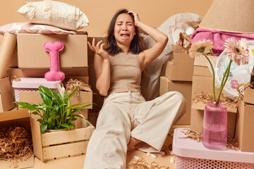 Upset crying young Asian woman feels unhappy dressed in t shirt and trousers relocates to new apartment surrounded by cardboard boxes full of personal belongings feels tired of packing things