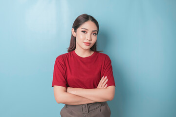 Obraz premium Portrait of a confident smiling girl standing with arms folded and looking at the camera isolated over blue background, wearing a red t-shirt