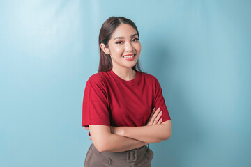Obraz premium Portrait of a confident smiling girl standing with arms folded and looking at the camera isolated over blue background, wearing a red t-shirt