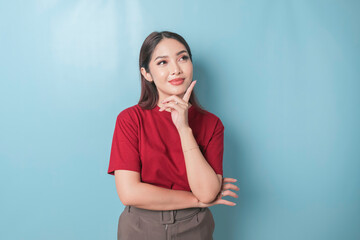 Portrait of a thoughtful young casual girl wearing a red t-shirt looking aside isolated over blue...