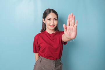 Young Asian woman wearing red t-shirt over blue isolated background doing stop sign with palm of the hand.