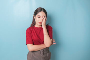 A portrait of an Asian woman wearing a red t-shirt isolated by blue background looks depressed