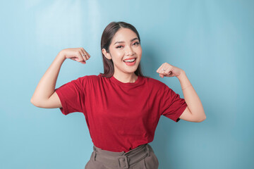 Excited Asian woman wearing a red t-shirt showing strong gesture by lifting her arms and muscles smiling proudly