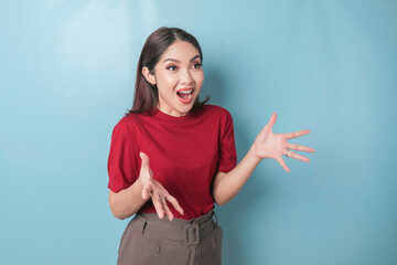 A portrait of a surprised Asian woman wearing a red t-shirt isolated by blue background