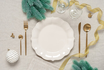 Christmas table setting. Empty beige plate with golden cutlery and Xmas decorations. Top view, flat...
