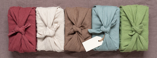 Gifts wrapped in colored cloth. Furoshiki gifts in a row on a brown background. Reusable sustainable gift wrapping. Zero waste concept. Top view, flat lay. Banner