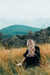 a girl sits in a field and looks at the mountains
