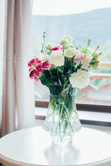 .a bouquet of flowers in a transparent vase on the table against the background of the window