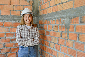 Portrait of Young Asian engineer or foreman female wearing white safety helmet and arms crossed posing with building construction site as the background.