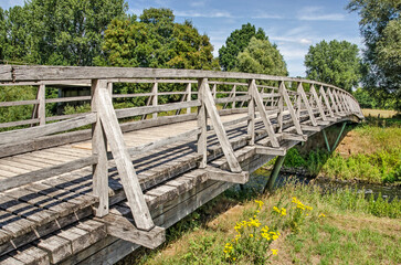 Munster, Germany, July 28, 2022: weathered wooden bridge across the river Ems in a green landscape on a sunny day in summer