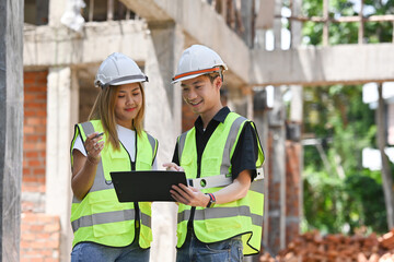 Fototapeta premium Two Asian male and female architects or engineers standing with checking on blueprint in front of construction site as the background.