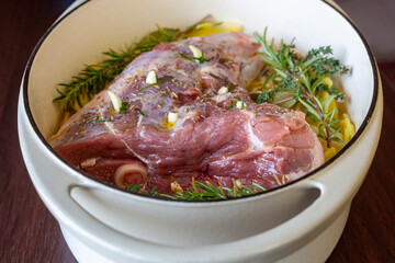Raw leg of lamb prepared to cook with sliced potatoes and provencal herbs