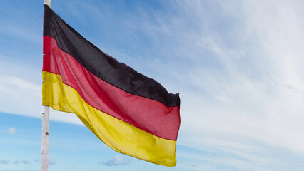 The official flag of Germany waving on a blue sky background. Horizontal banner design, with the German flag hanging on a sunny background with white clouds. Deutschland flag wide banner