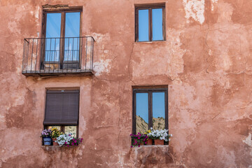 Fototapeta na wymiar Windows and balconies adorned with plants, on a brown stucco wall.