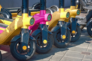 Electric scooter parked in row, rental electrical scooter. Pink scooter among yellow ones. Charged electric scooters for rent. Electric scooters for rent in the parking lot. Eco-friendly transport
