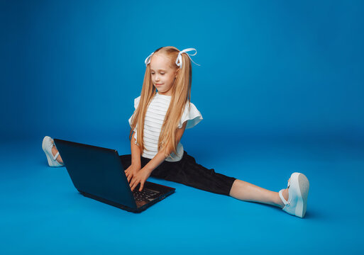 a schoolgirl is sitting on a blue background and looking at a laptop. a little girl is studying online. the child is typing on a laptop. isolated background.