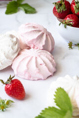 Red and white marshmallows on a white background next to a bowl of strawberries