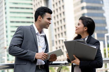 Indian businessman talking with businesswoman colleague outdoors with city office buildings in background