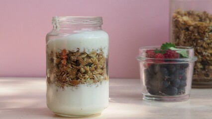 The girl prepares a delicious breakfast with yogurt, muesli, porridge and berries. environmentally friendly products. fresh fruits and berries. vitamins. jar granola