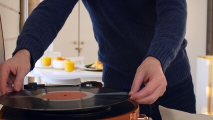 A man puts a vinyl record into a player and turns it on. The record spins and the man lowers the needle to read the music. Listening to music at home alone, classical music from the gramophone.
