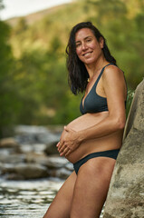 Relaxed pregnant woman in the nature, enjoying a beautiful spot on a river shore.