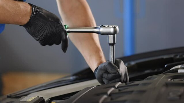 Close Up of male mechanic working on car in a Car Service. Empowering man makes an usual car maintenance. He's using a ratchet. Modern clean workshop. Auto service