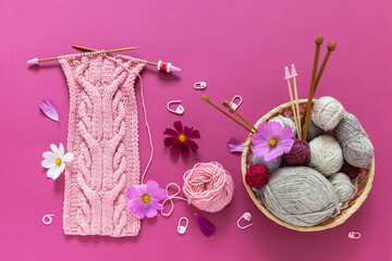 Wicker basket with skeins of yarn and a knitted headband with braids on a pink background. Summer...