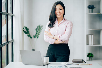 Confident young Asian business woman sitting with arms crossed smiling looking at camera in the office