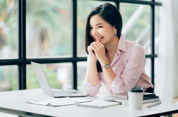 Obraz premium Charming Asian businesswoman working with a laptop at the office. Looking at camera