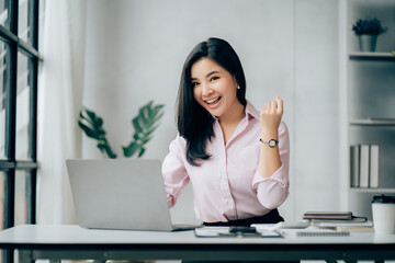 Happy young asian businesswoman sitting on her workplace in the office. Young woman working at laptop in the office