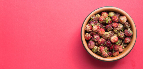 Fresh ripe red berries of wild forest strawberries in brown bowl. Top view. Red background.  Summer menu, natural vitamins