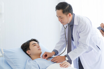 Obraz premium Senior doctor and young male patient who lie on the bed while checking pulse, consult and explain with nurse taking note and supporting in hospital wards.