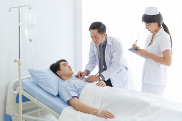 Obraz premium Senior doctor and young male patient who lie on the bed while checking pulse, consult and explain with nurse taking note and supporting in hospital wards.