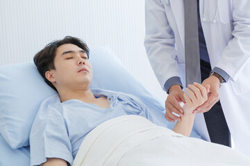 Fototapeta premium Senior doctor and young male patient who lie on the bed while checking pulse in hospital wards.